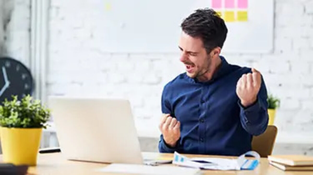 Man celebrating at desk with open laptop