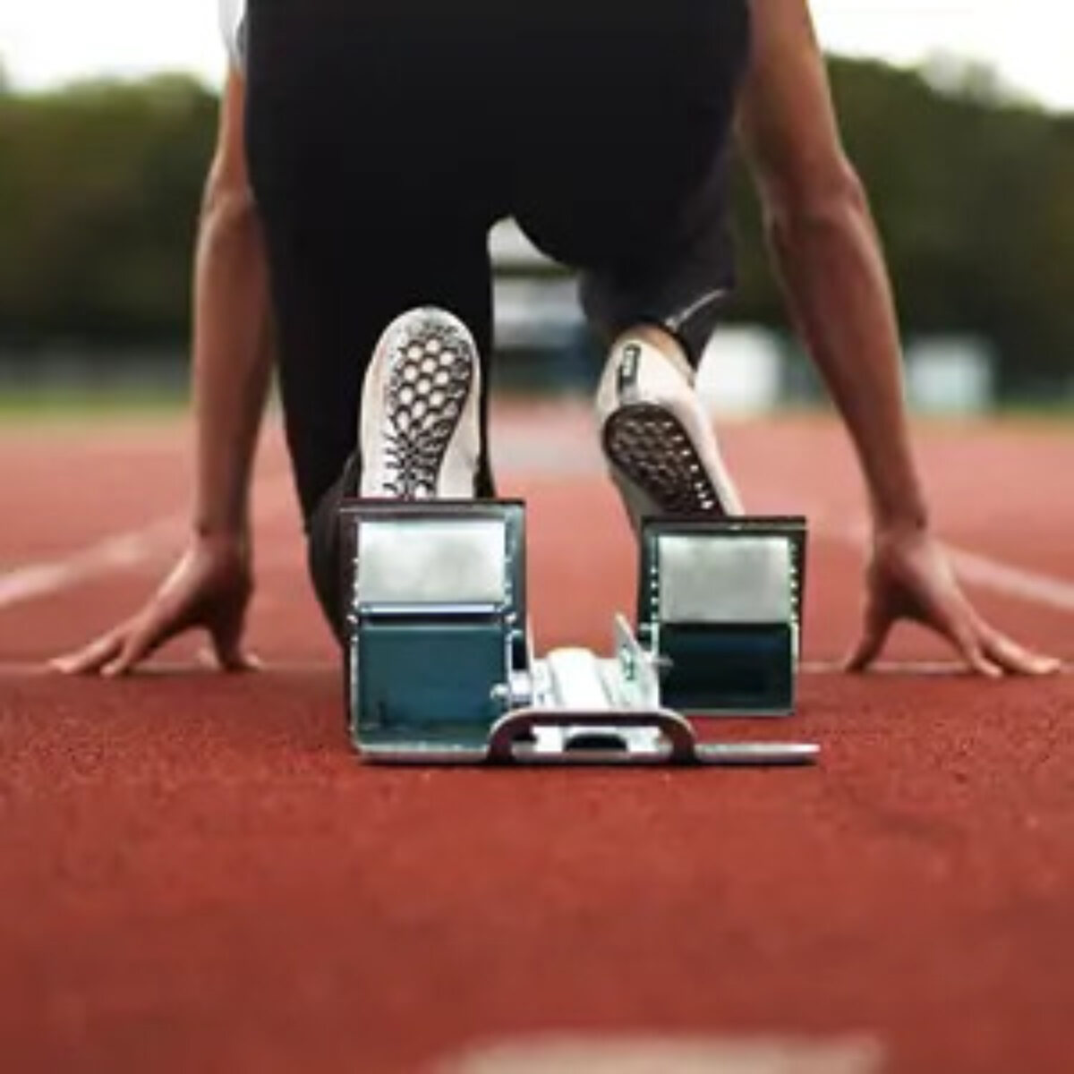 Runner kneeling at starting blocks of racetrack from behind