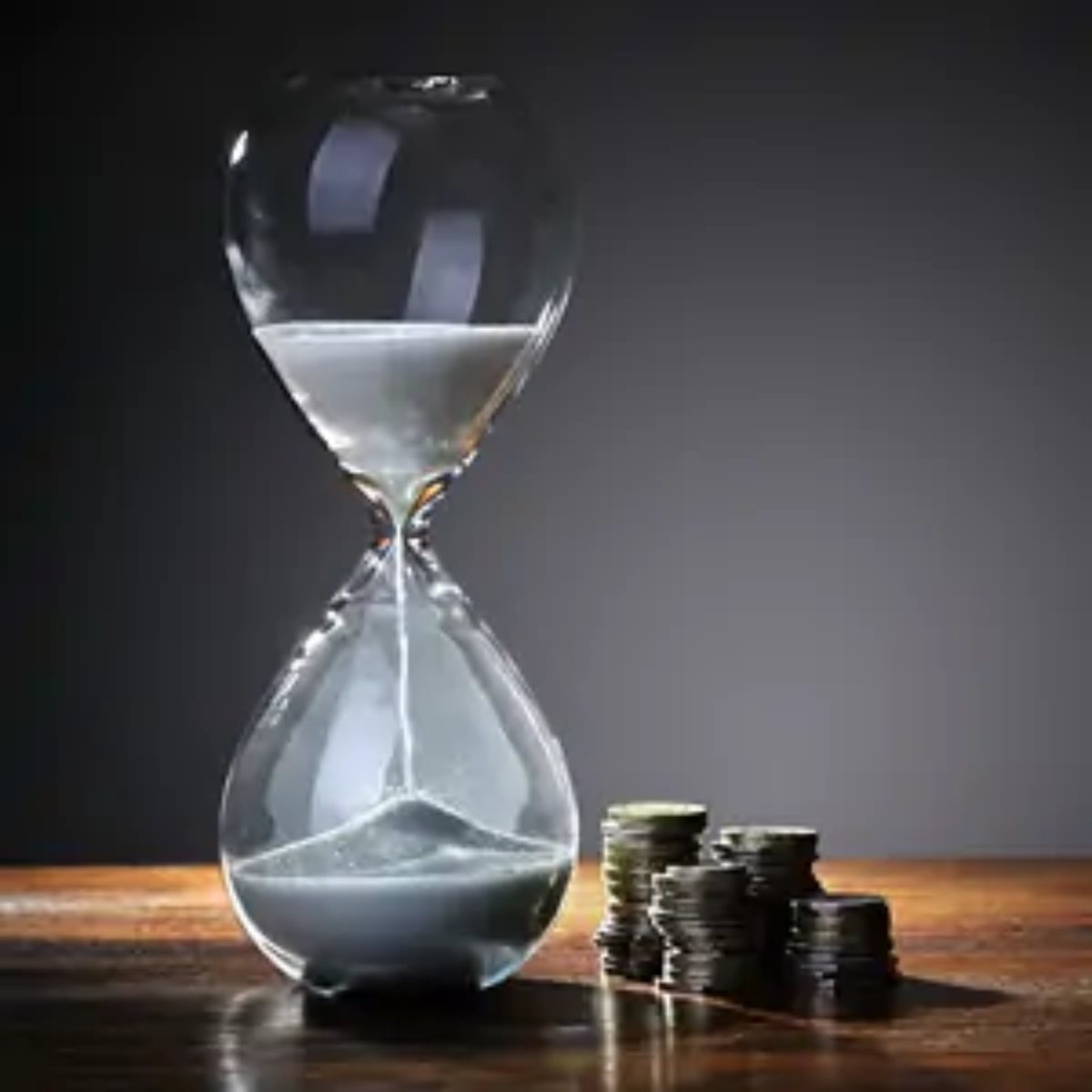 Sand timer halfway done next to four stacks of coins