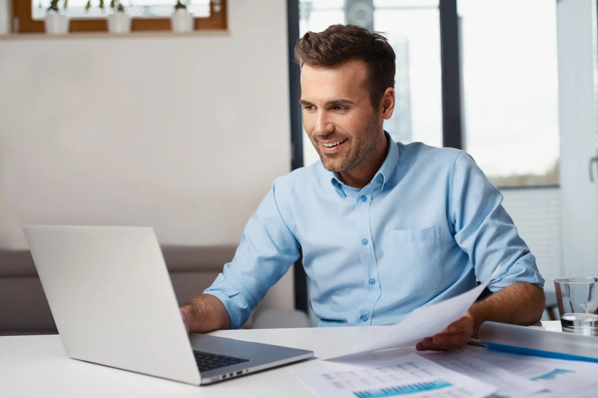 Businessman working on laptop and holding documents at desk