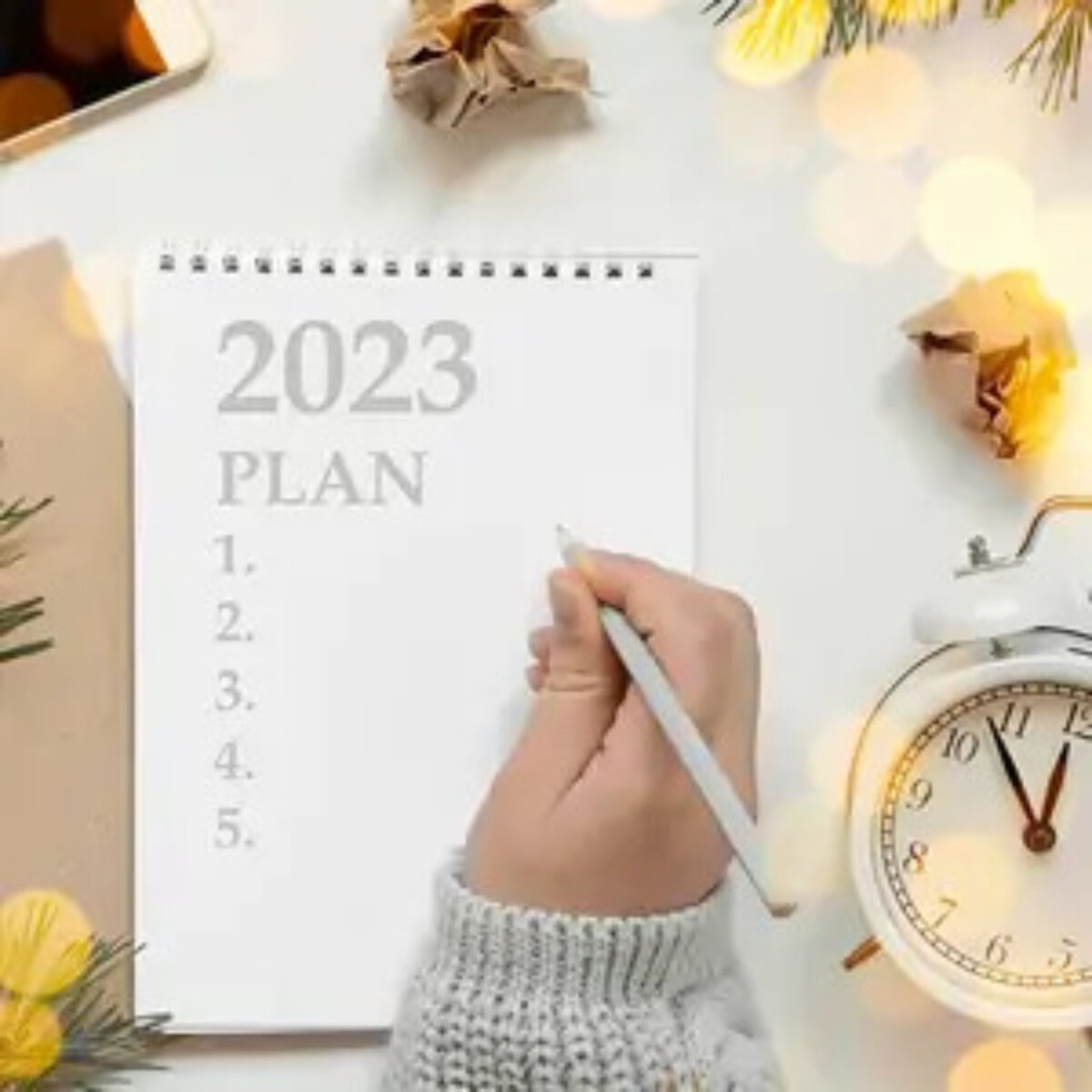 Woman's hand holding pencil over open notebook with '2023 business plan' and a list of numbers 1-5 written in it