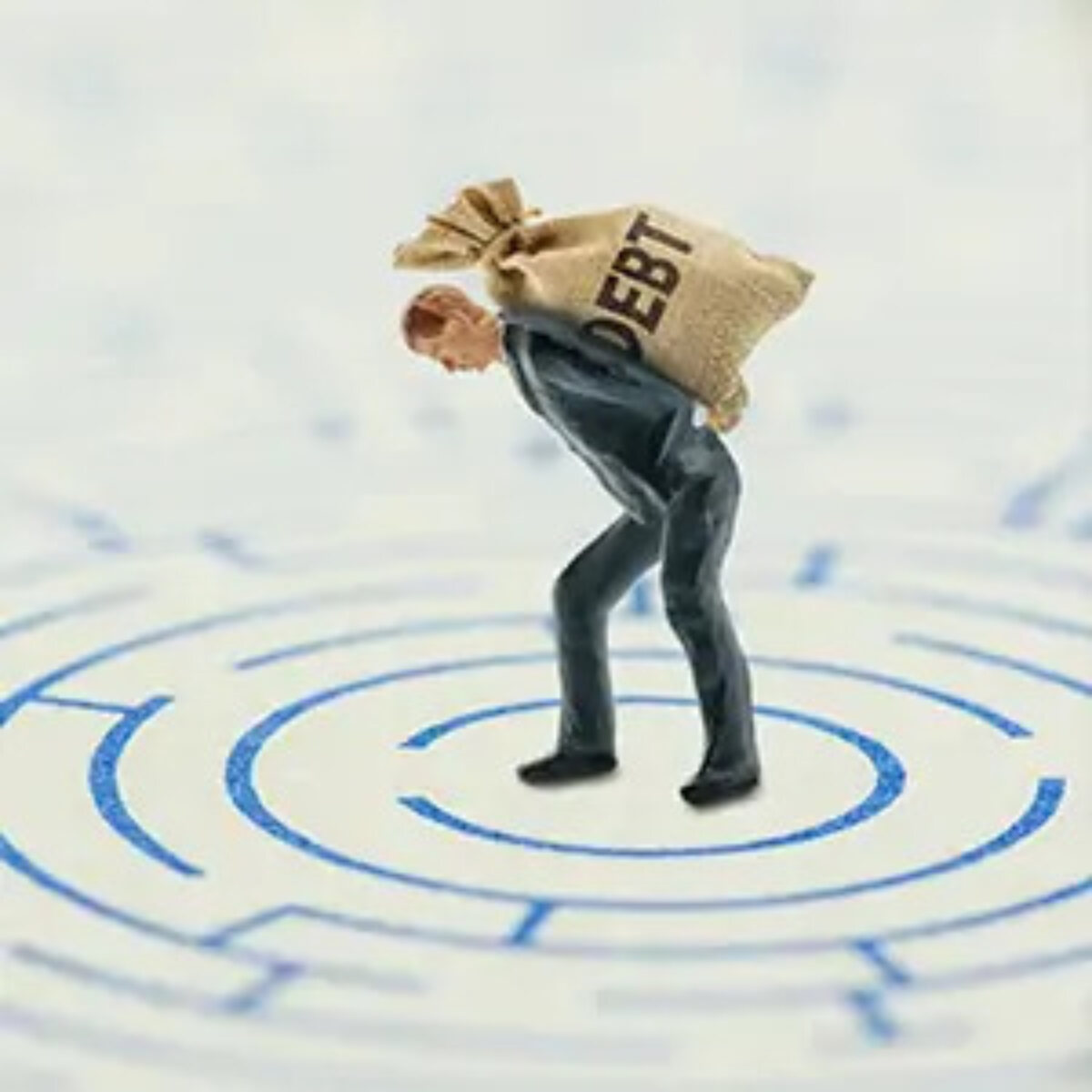 Figurine of a businessman hunched over with a sack saying 'debt' on his back in the centre of a maze