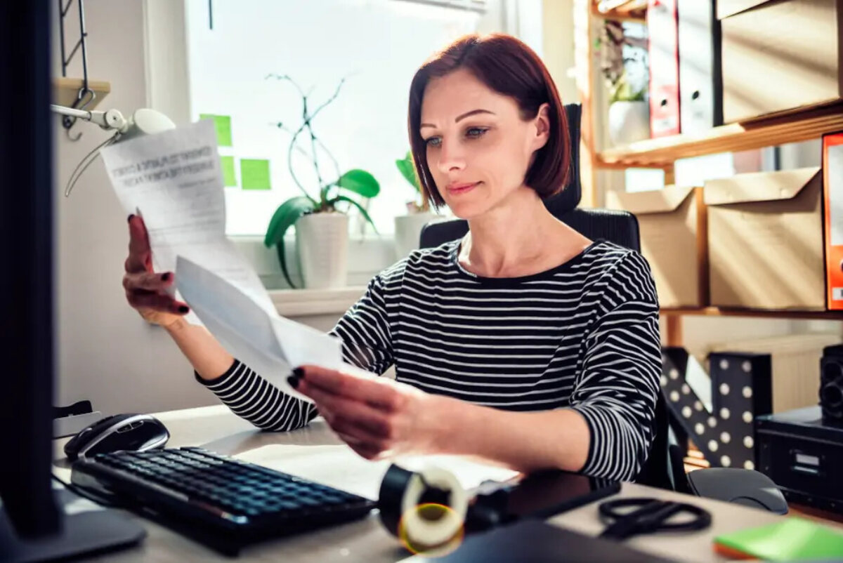 Businesswoman working from home reading letter in front of desktop