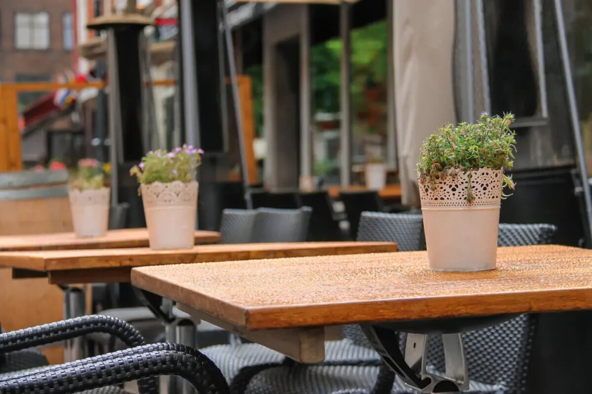 Pavement cafe tables and chairs with a plant on top of each table