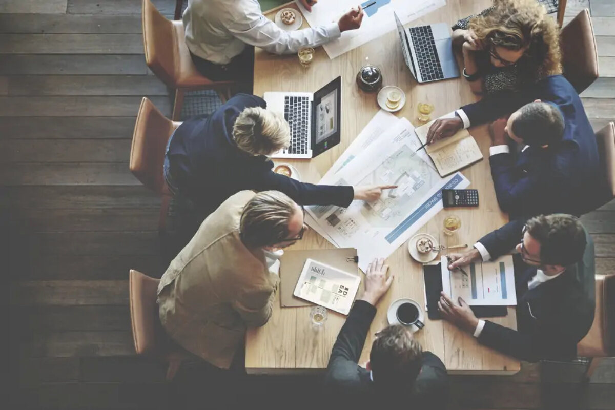 Businesspeople sitting around table at meeting with laptops discussing documents