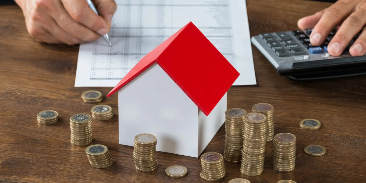 Businessman doing calculations beside a model house and stacks of coins