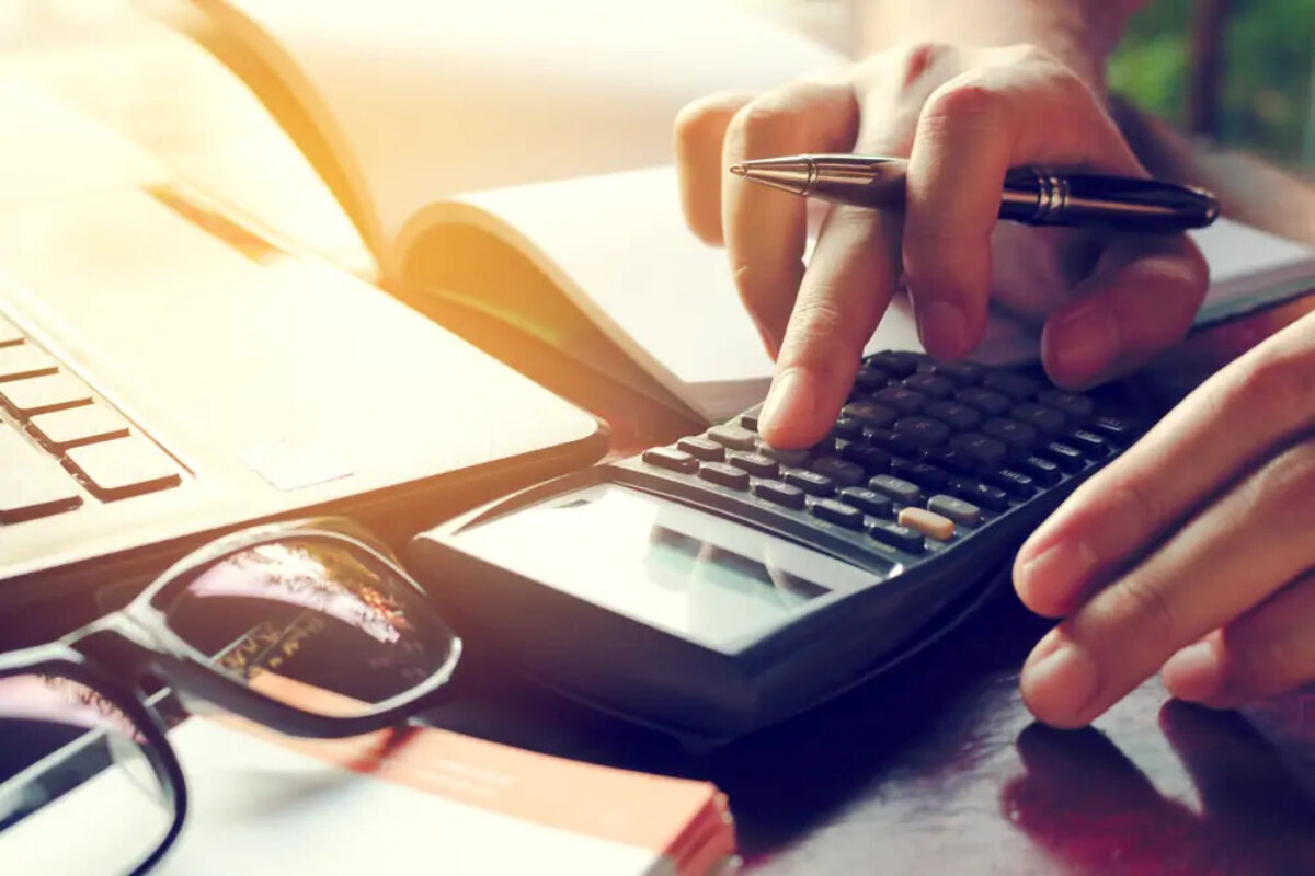 Businessperson at desk holding pen and using calculator to work out debt sums