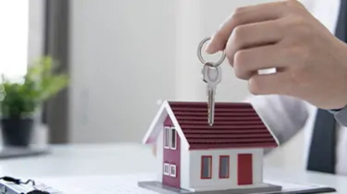Hand holding a set of keys over a model house