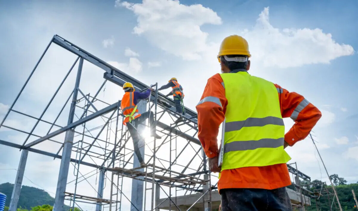 Two subcontractors working on scaffolding at construction site and one subcontractor standing watching them