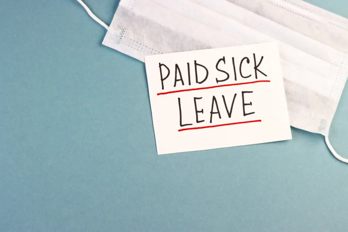 Piece of paper with 'paid sick leave' written on it on top of face mask