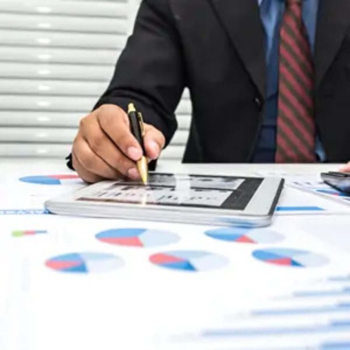 Businessman tapping tablet with stylus on desk covered in sheets of pie charts