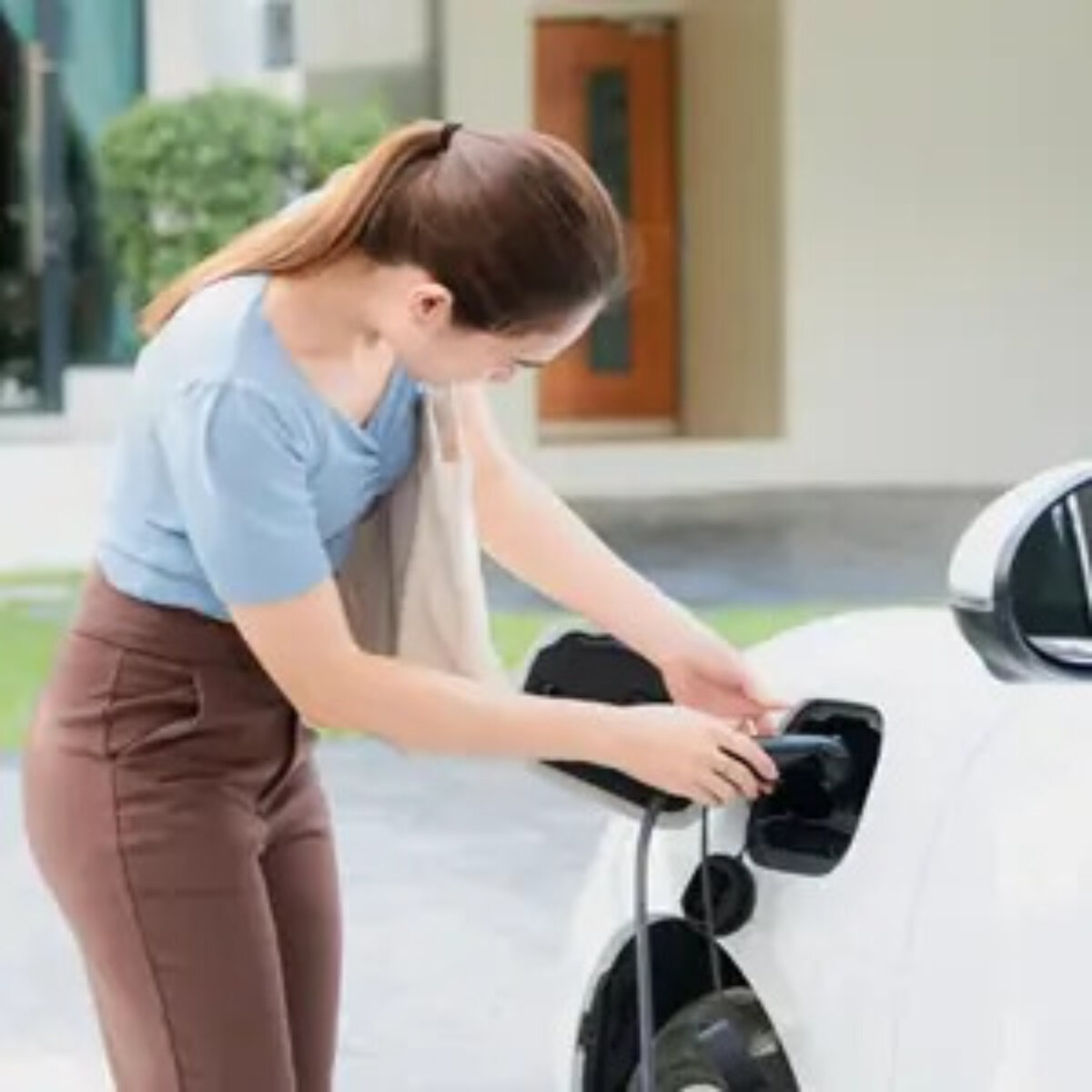 Woman connecting charger to electric car outside house