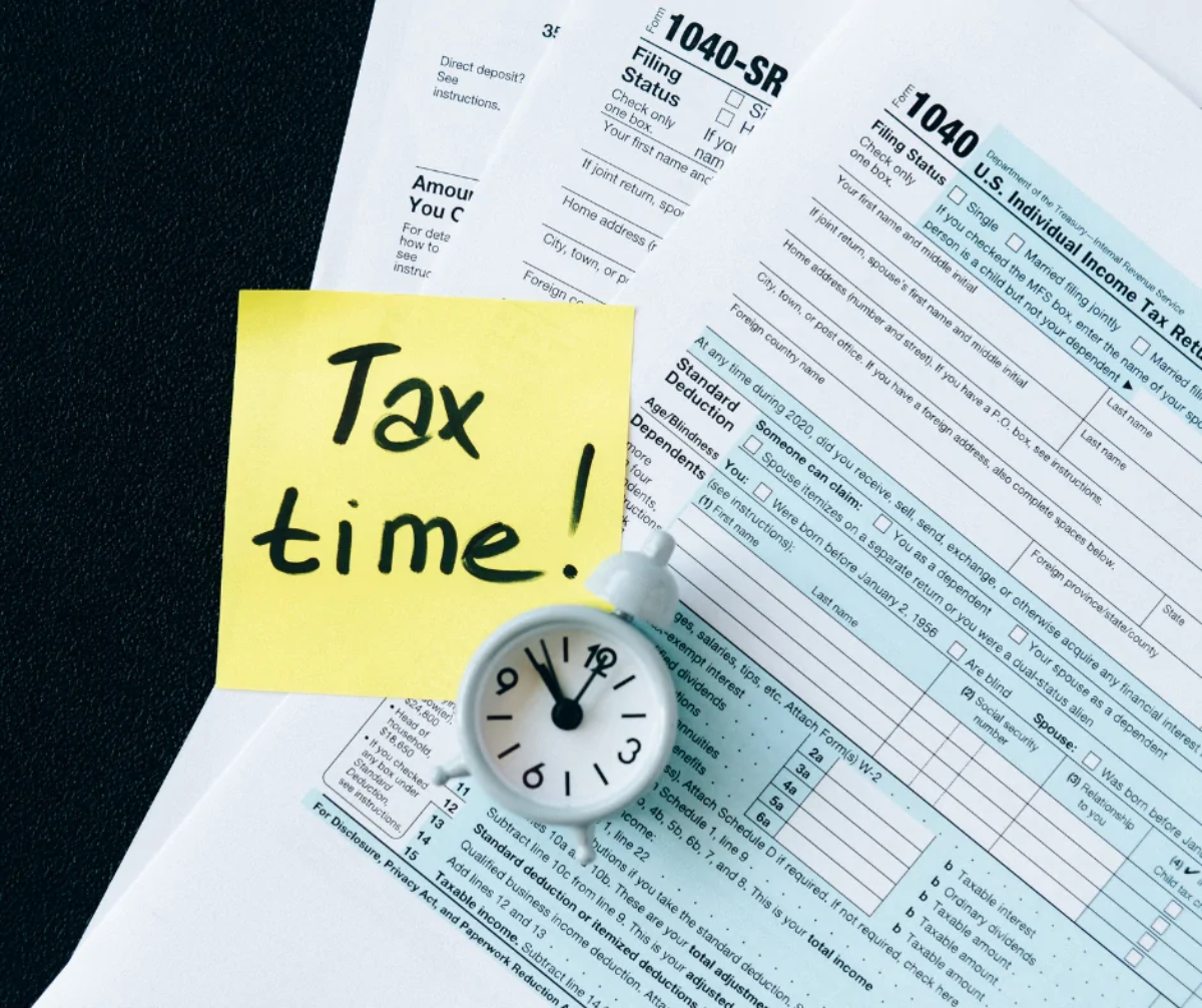 Tax return form with an alarm clock sitting on top and a post-it note reading 'Tax time!'
