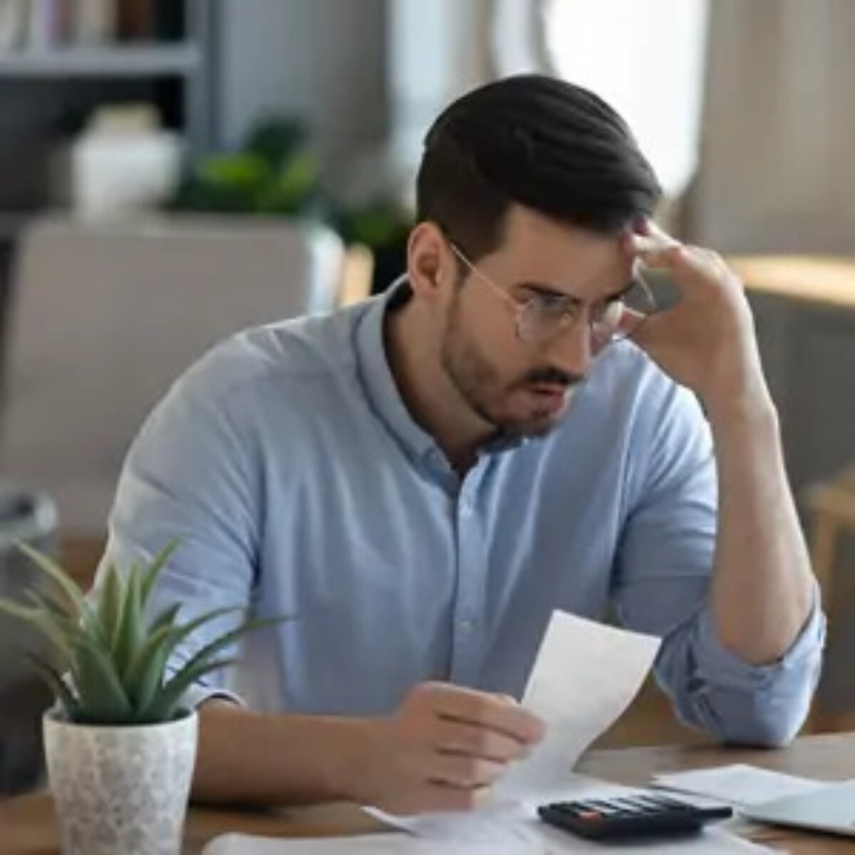 Businessman with hand to forehead holding a document at desk