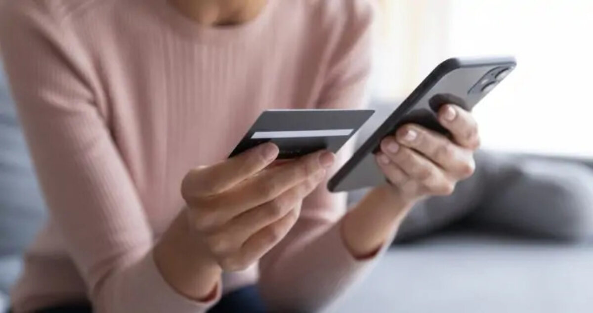 Woman sitting on sofa holding up bank card next to smartphone