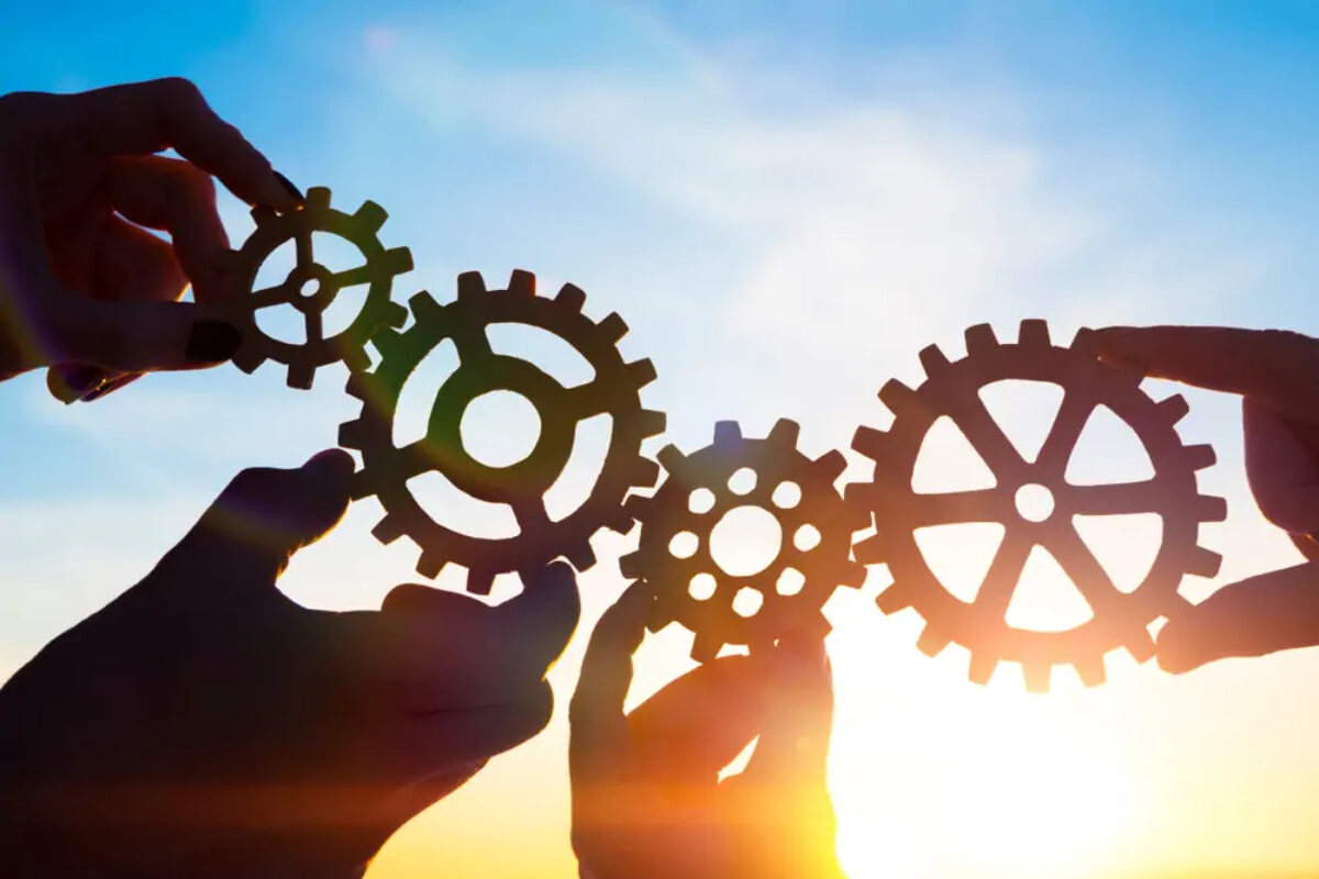 Four hands holding cogs with sun shining behind