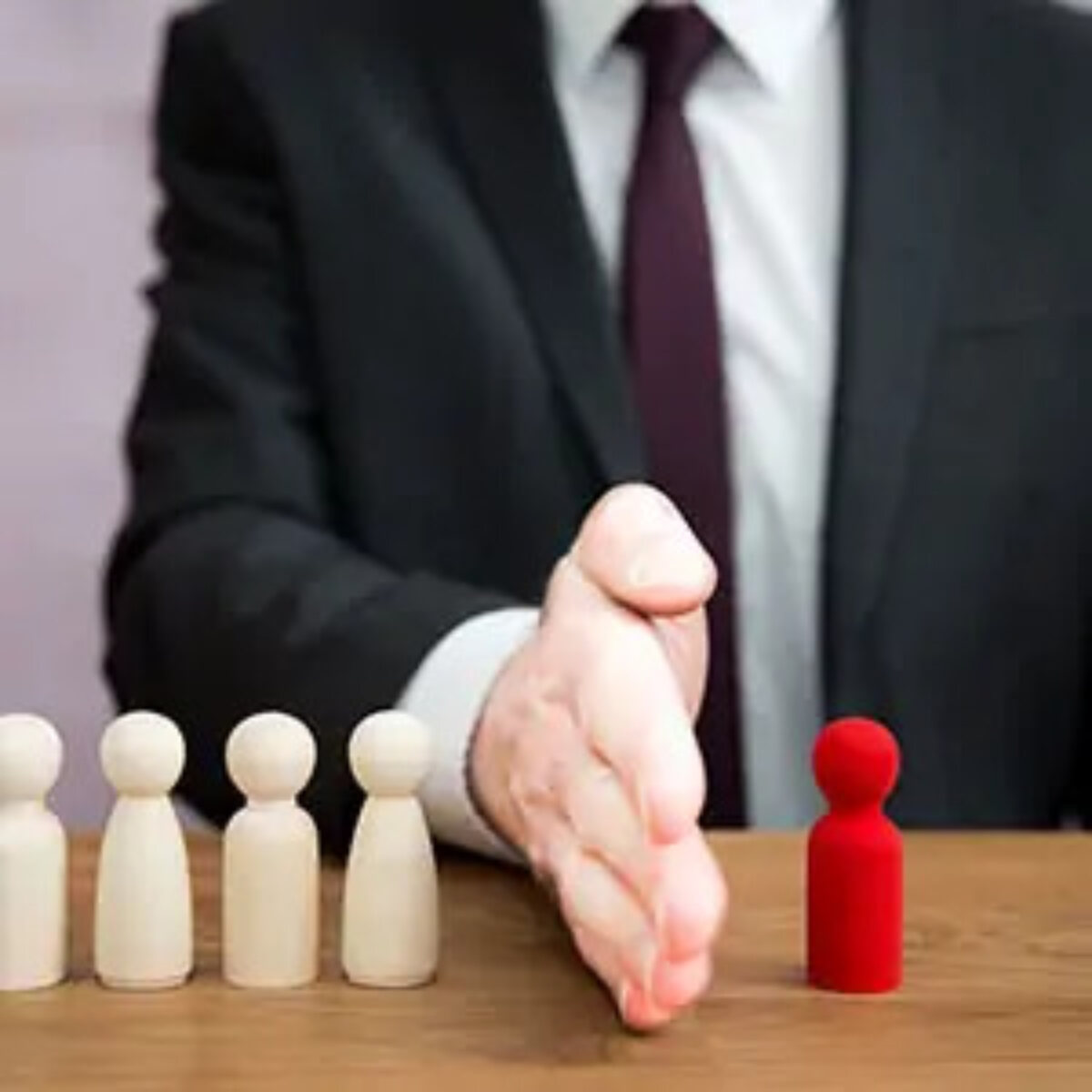 Businessman at table with hand out sideways separating four white figurines from one red figurine