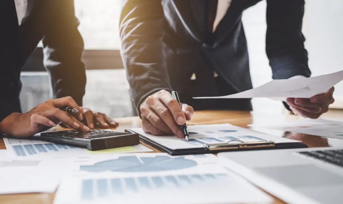 Two businessmen standing at desk looking at documents and making Corporation Tax calculations
