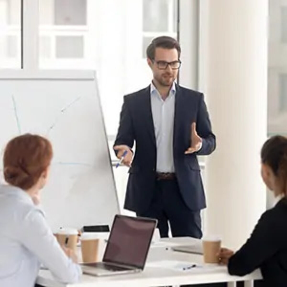 Businessman standing at flipchart talking to two seated colleagues