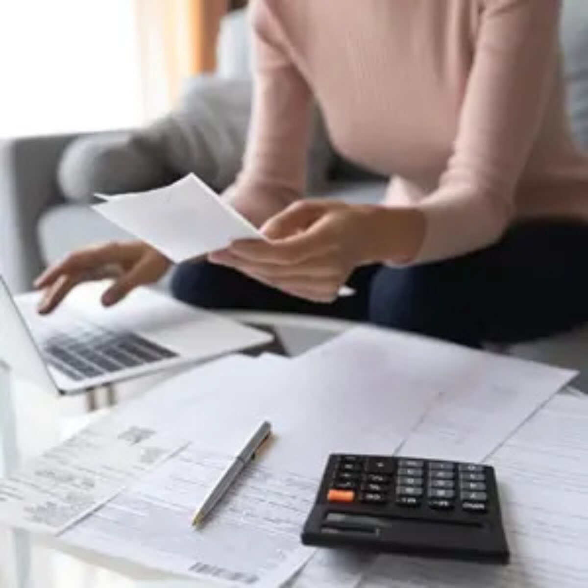 Woman sitting on sofa using laptop on coffee table calculating tax bill