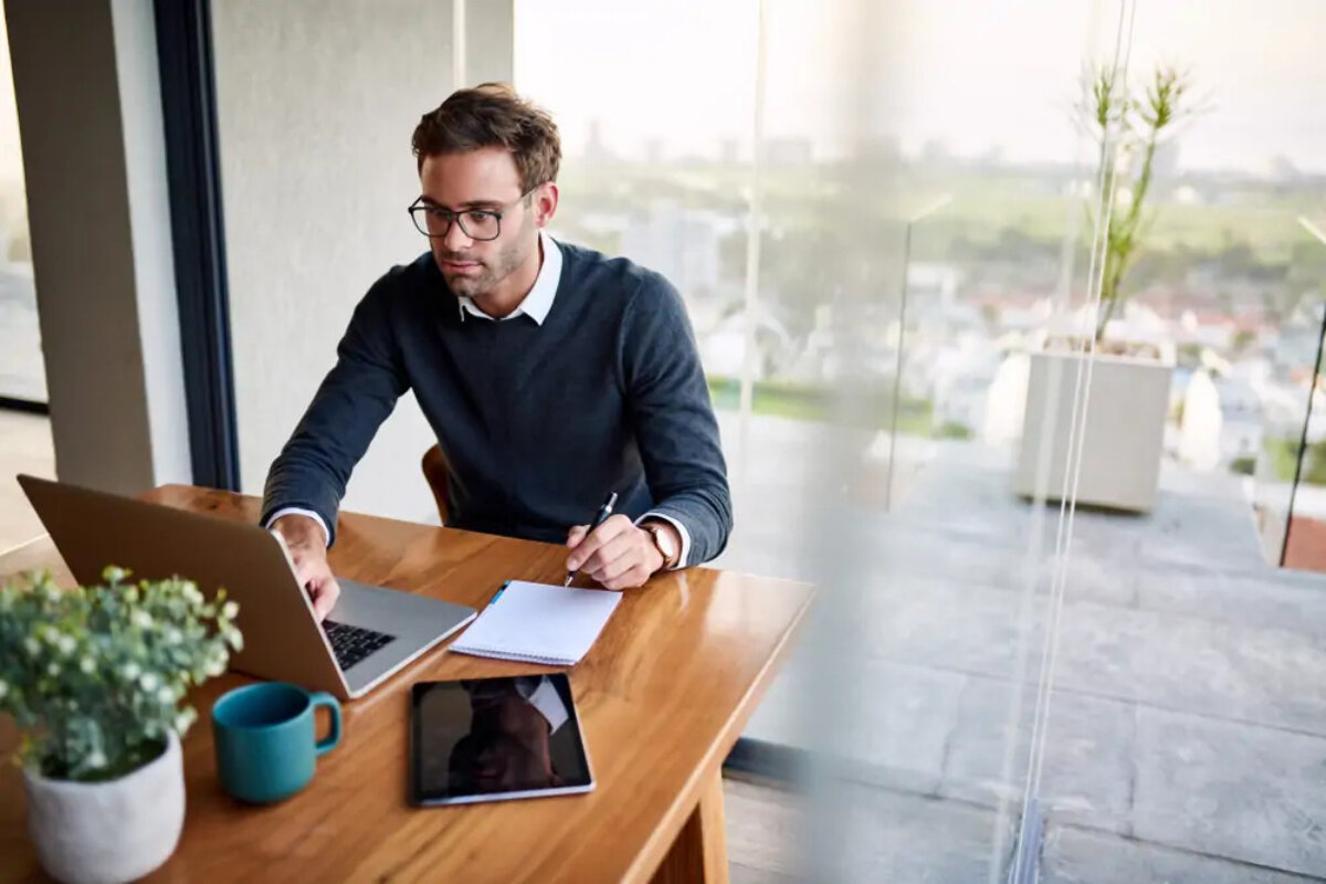 Businessman working on laptop and notebook and pen at desk next to tablet