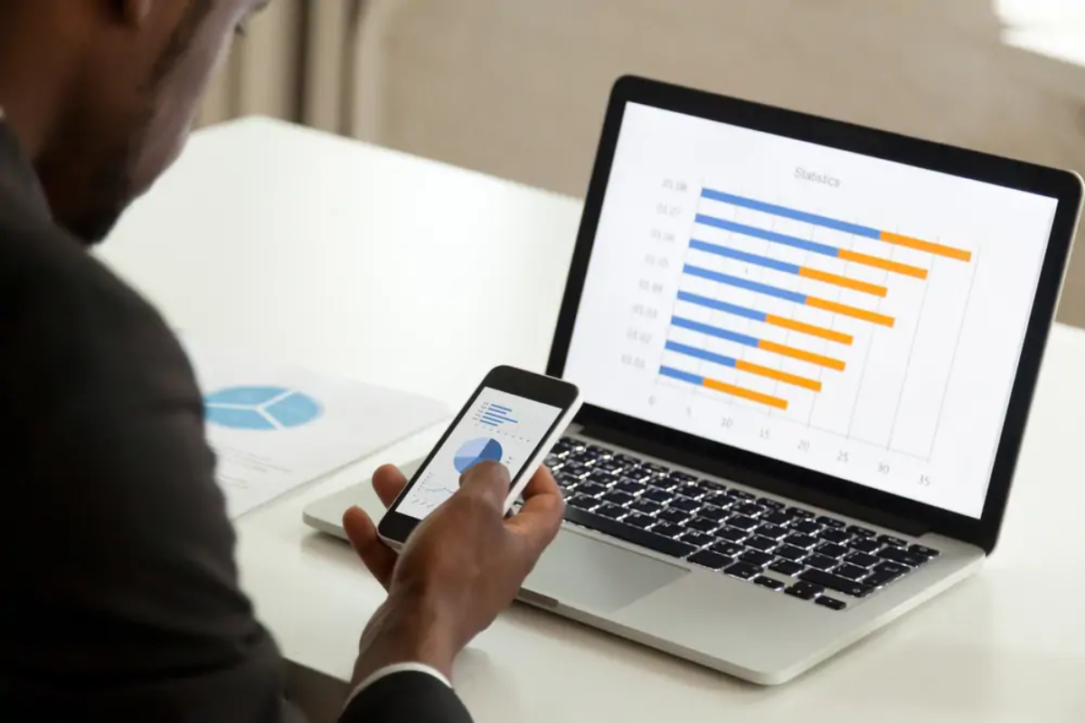 Businessman at table using smartphone in front of open laptop for cloud accounting