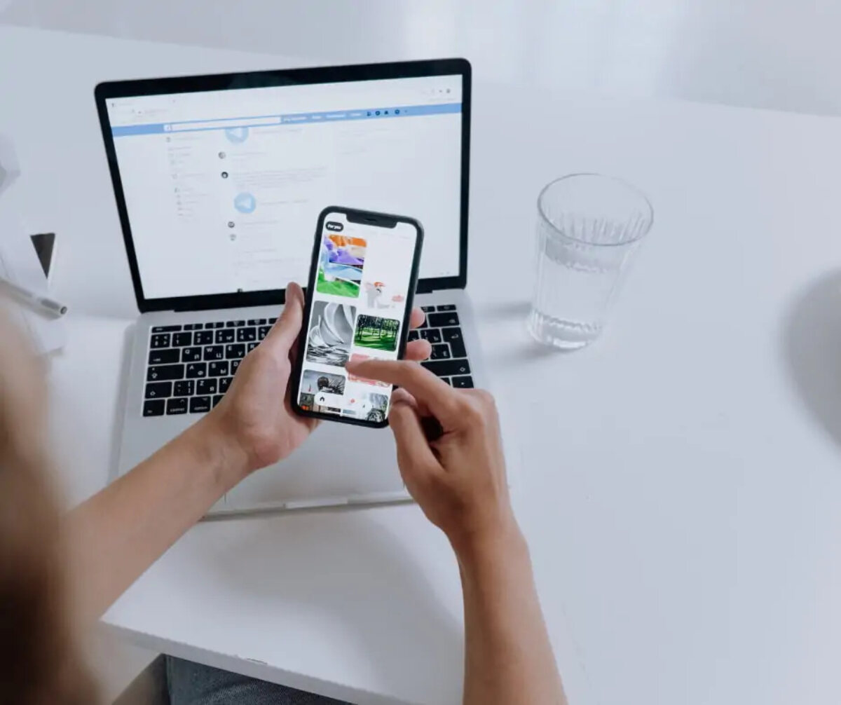 Person using a smartphone at desk in front of an open laptop