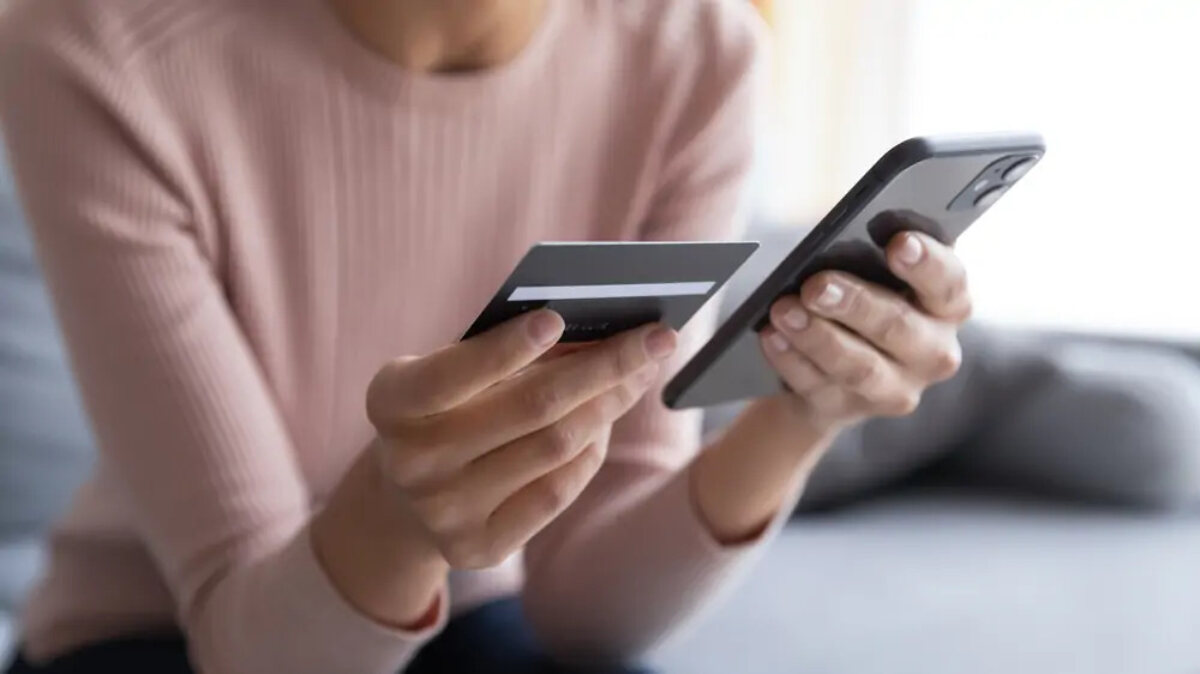 Woman sitting on sofa holding up bank card next to smartphone
