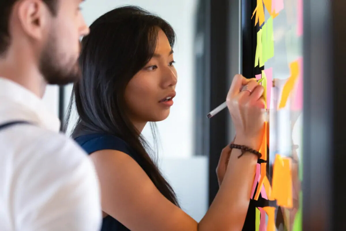 Businesswoman writing on post-it notes on wall t generate ideas for business goals