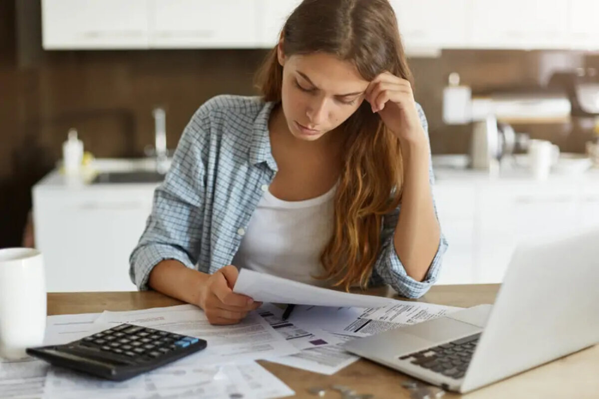 Woman reading document in front of laptop, calculator and more documents on desk