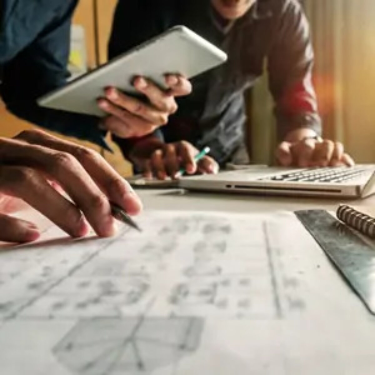 Two businessmen working on a tablet and laptop looking at a paper document on desk