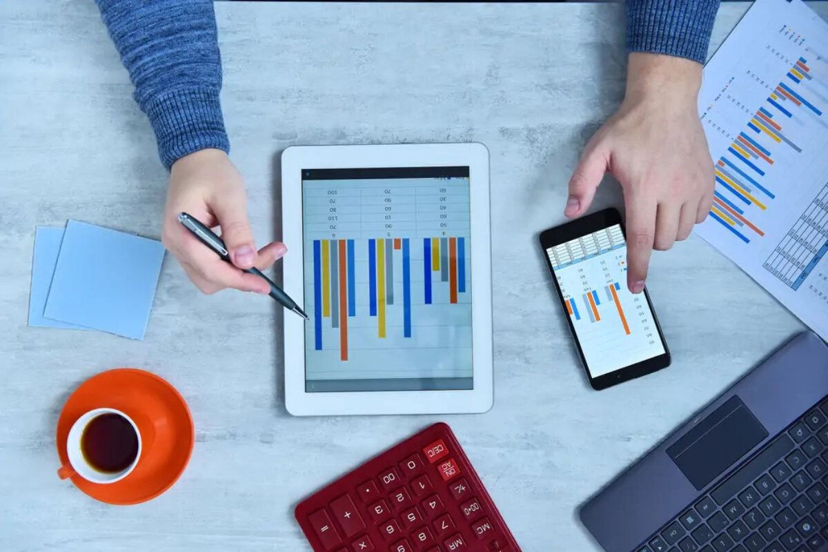 Businessman holding pen to tablet showing bar chart with one hand and using smartphone displaying similar bar chart with the other