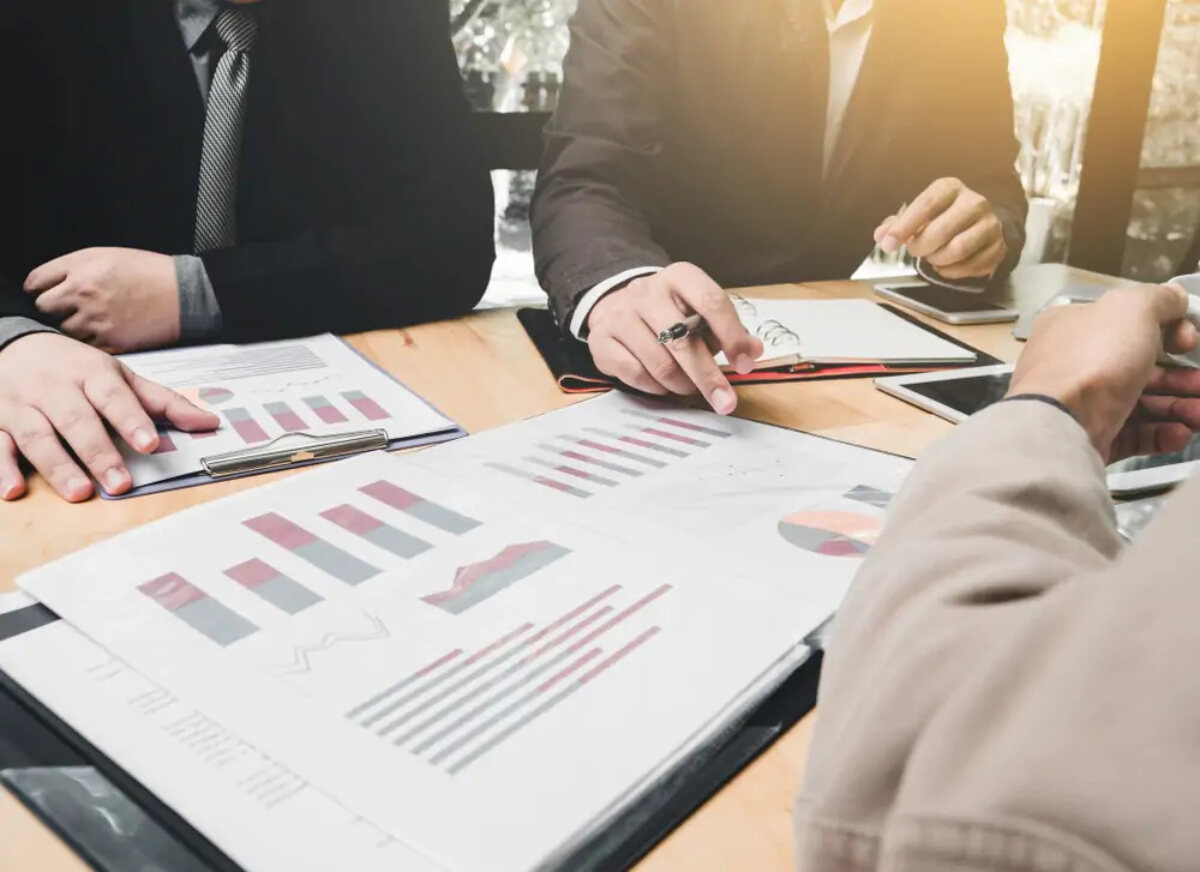 Businessmen in meeting pointing at documents displaying graphs and charts