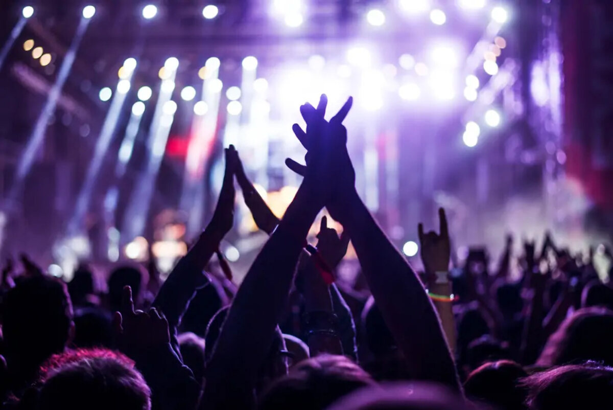 Audience with hands raised at concert with bright lights