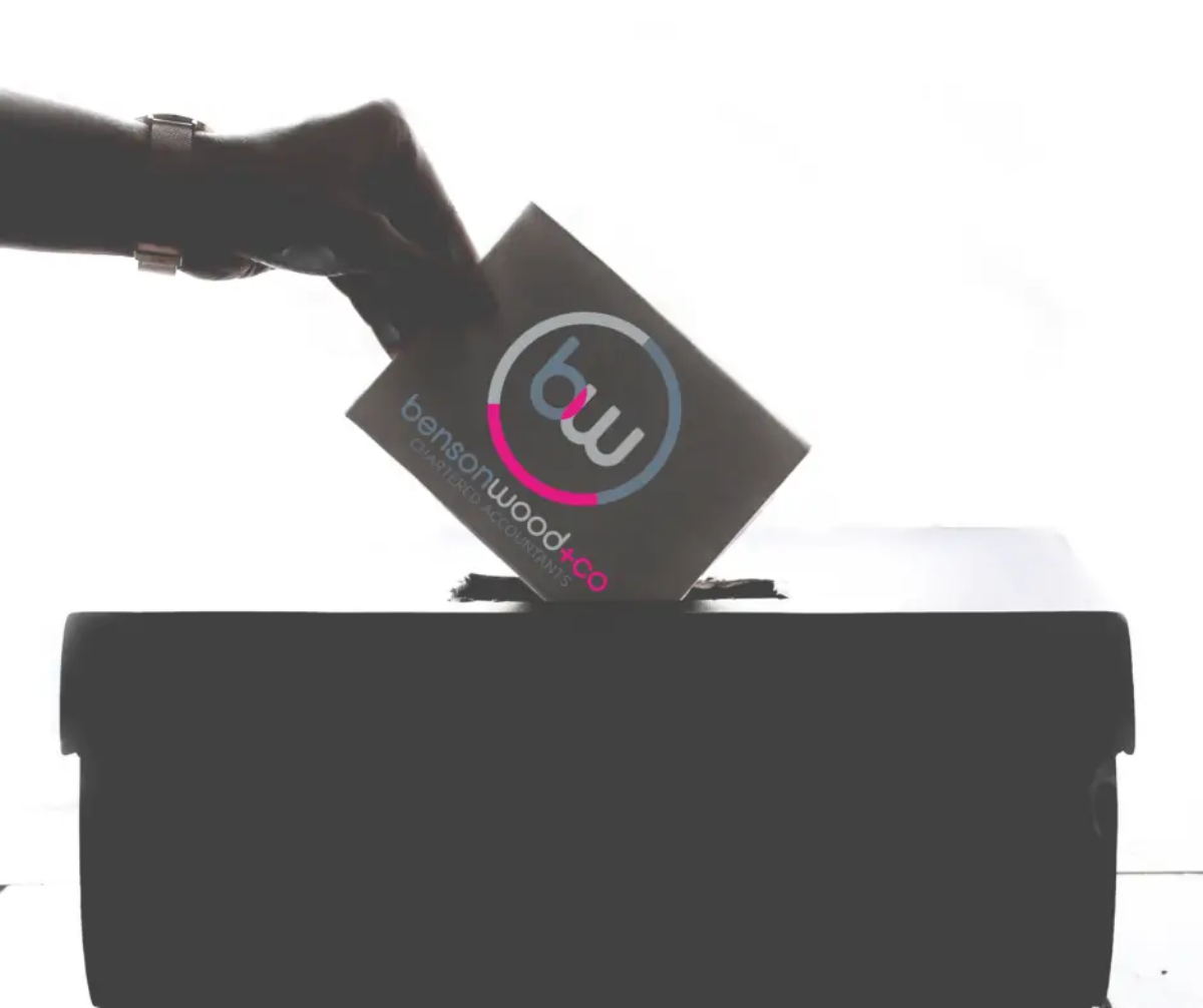 Hand inserting voting slip with Benson Wood & Co Chartered Accountants on it into ballot box