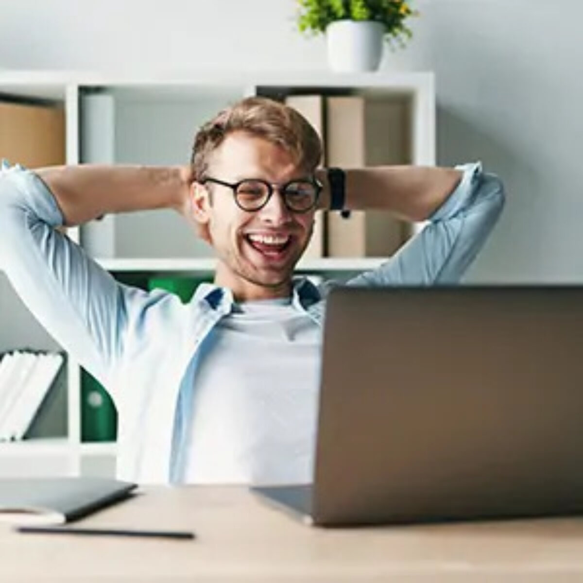 Businessman at desk smiling at laptop with hands behind head