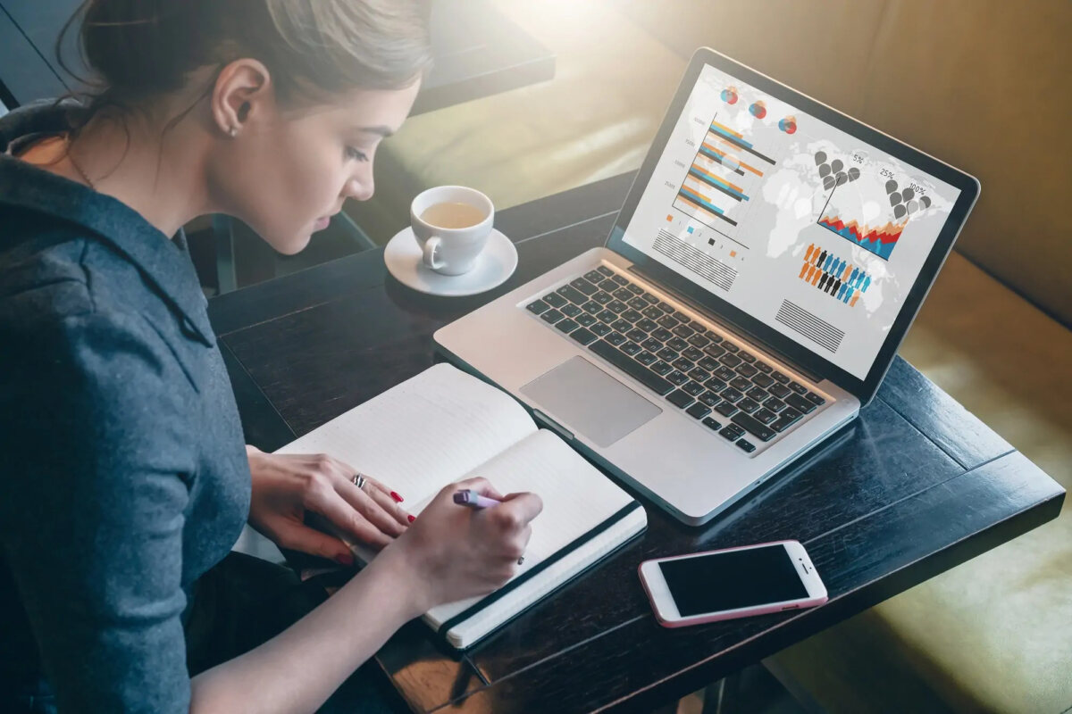 Businesswoman writing in a notebook next to mobile and laptop in a coffee shop