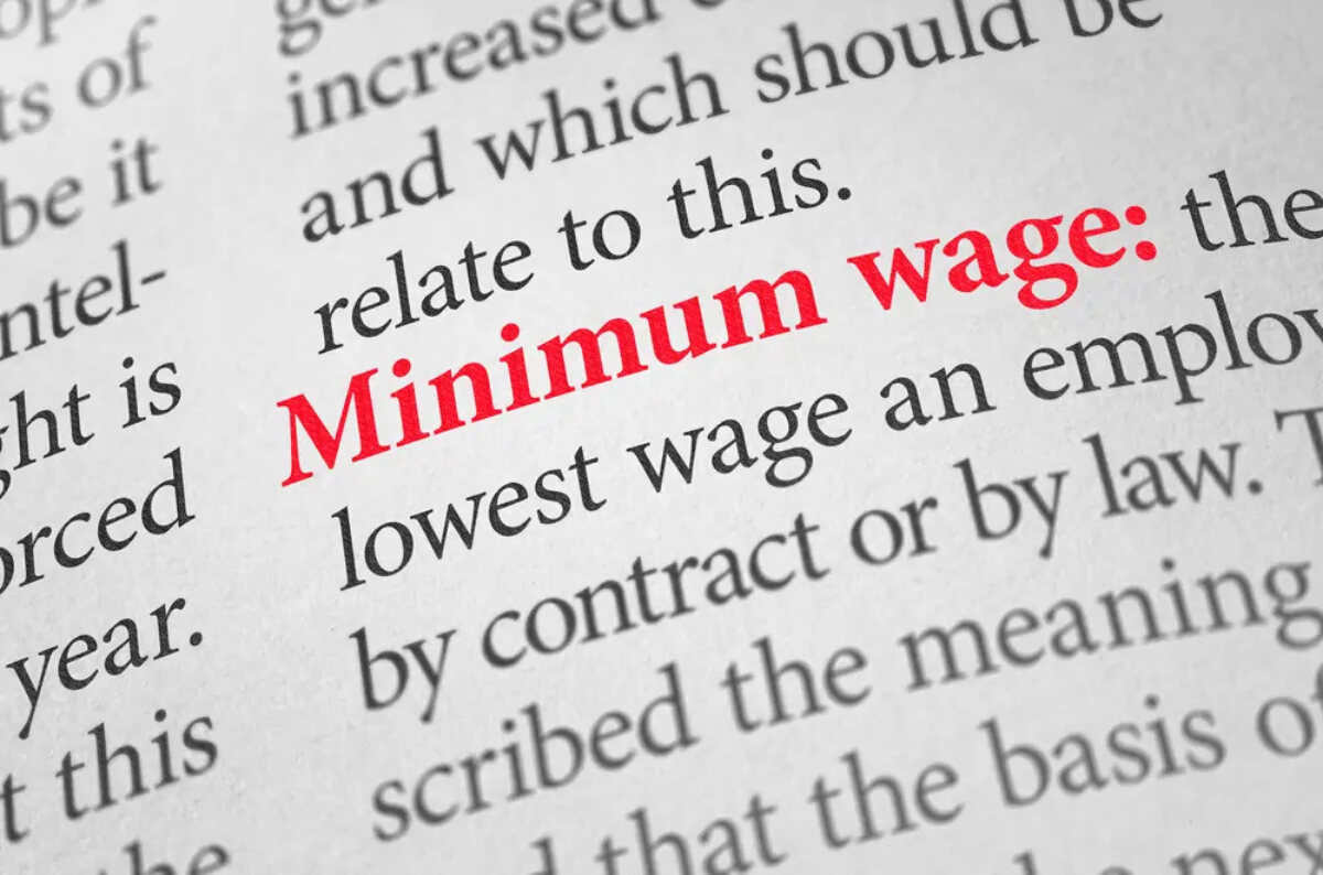 The words 'minimum wage' highlighted in bold and red text in a dictionary among other words on the page