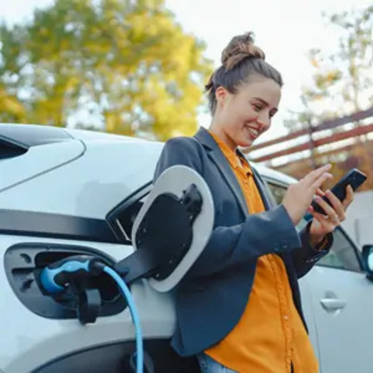 Woman using smartphone and smiling next to charging electric car
