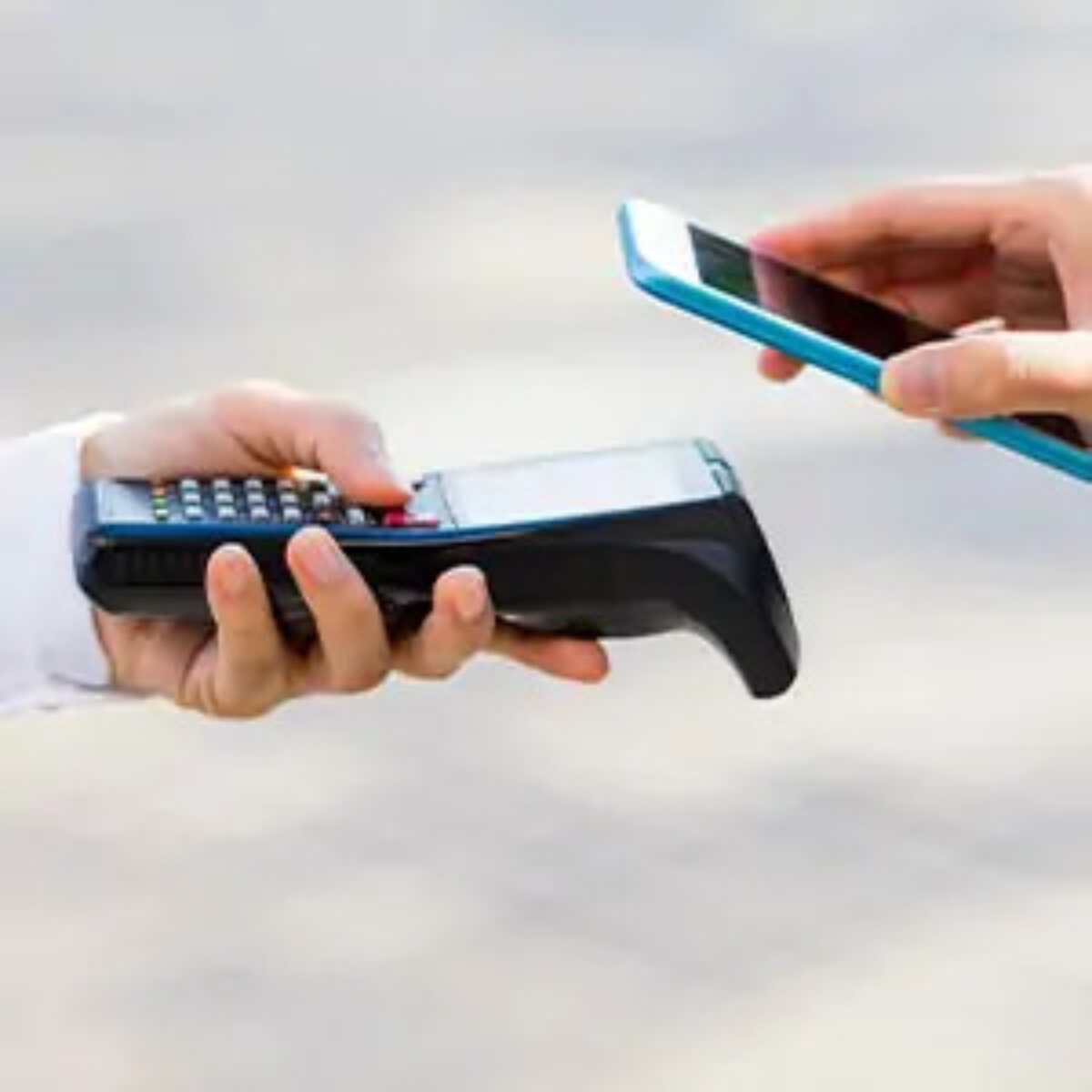 A hand holding a card machine and a hand holding a phone above it to make a contactless payment
