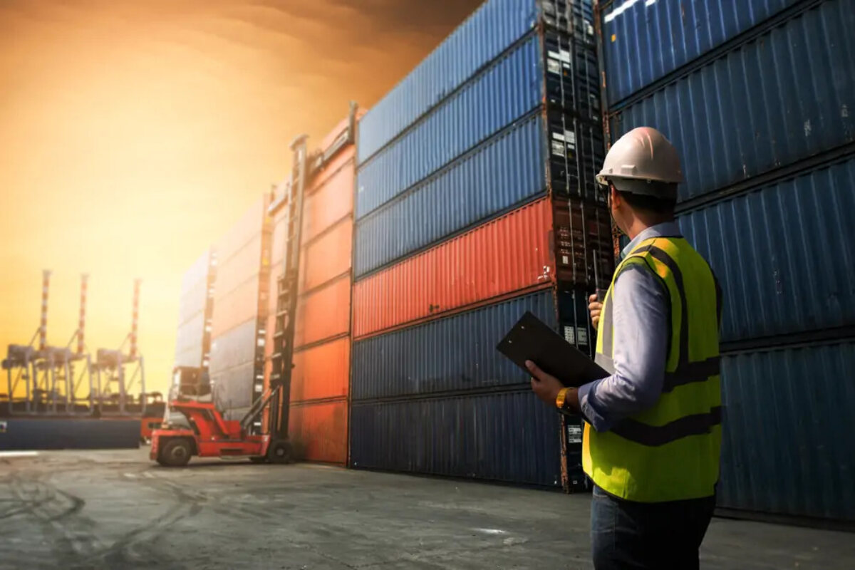 Man wearing high-vis and hard hat instructing loading of containers to cargo ship