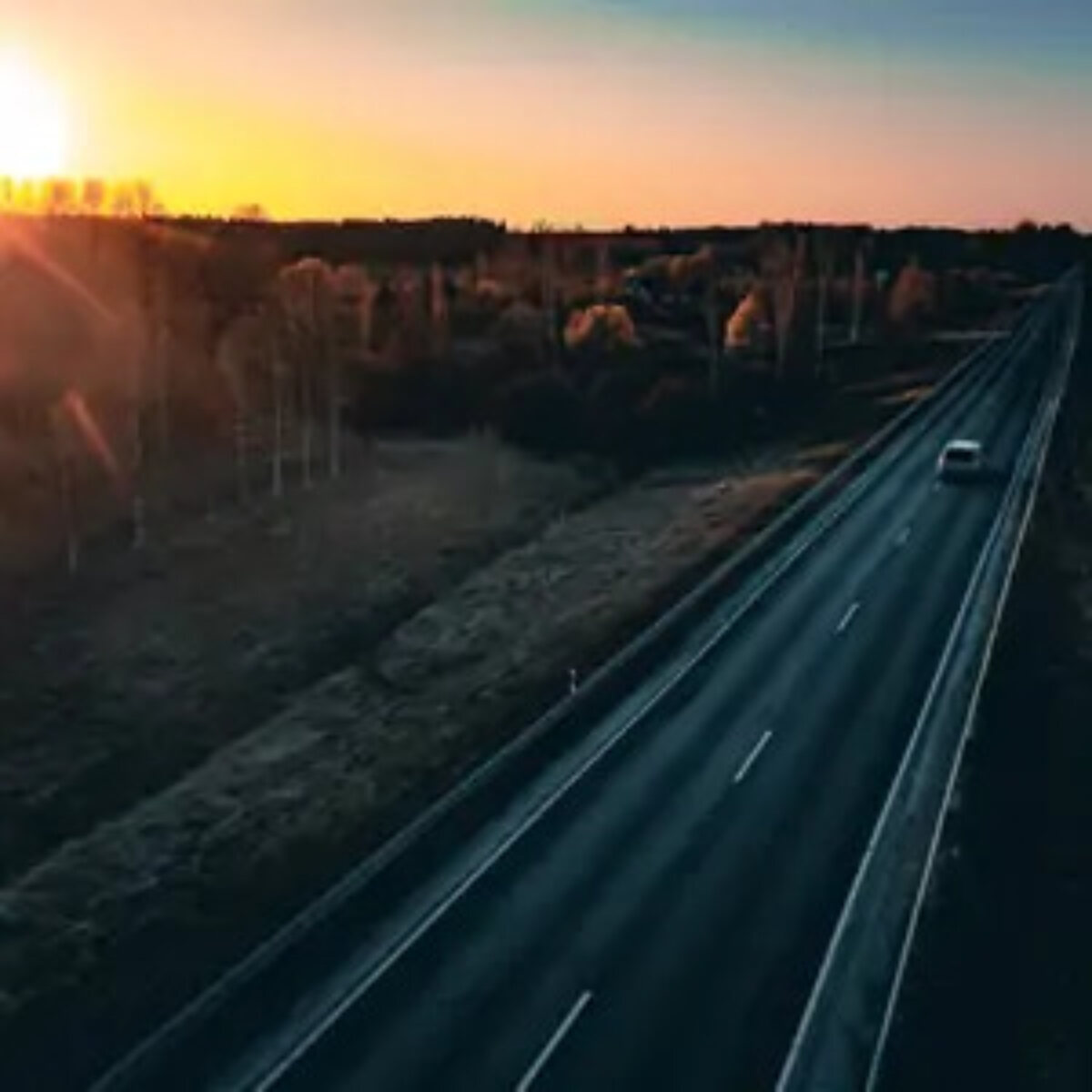 Single car on road through fields and trees at sunset
