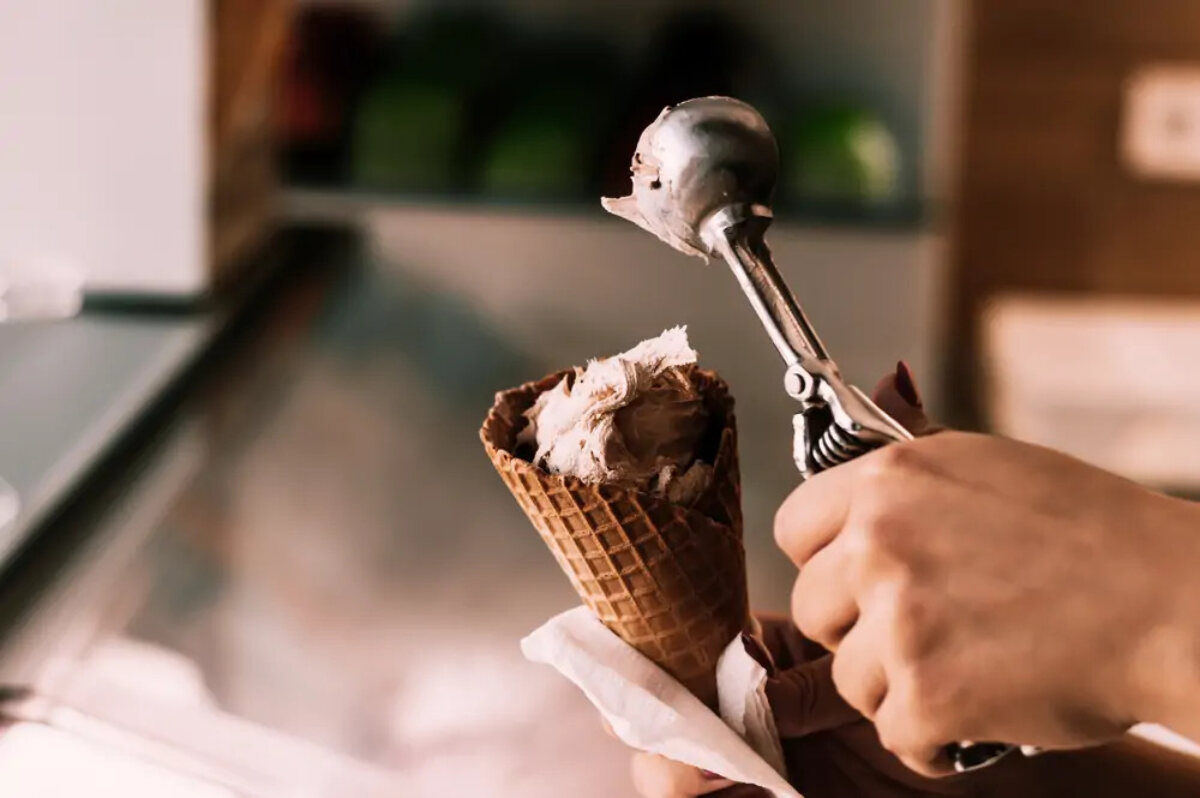 Hospitality worker scooping ice cream into a waffle cone