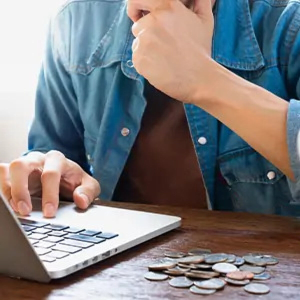 Man using laptop with pile of coins beside
