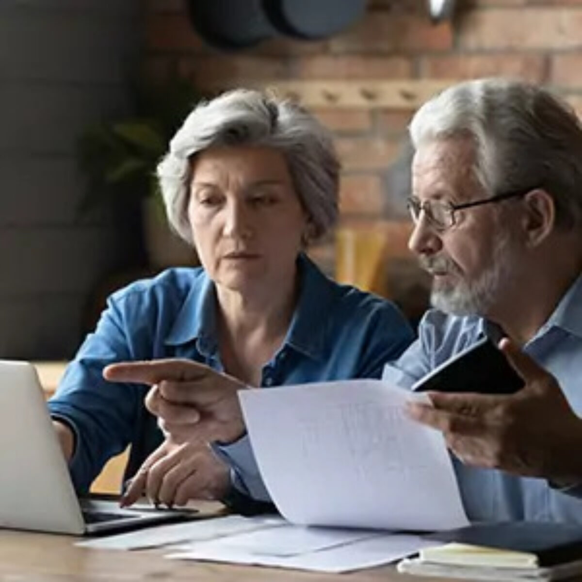 Two elderly people looking and pointing at laptop screen