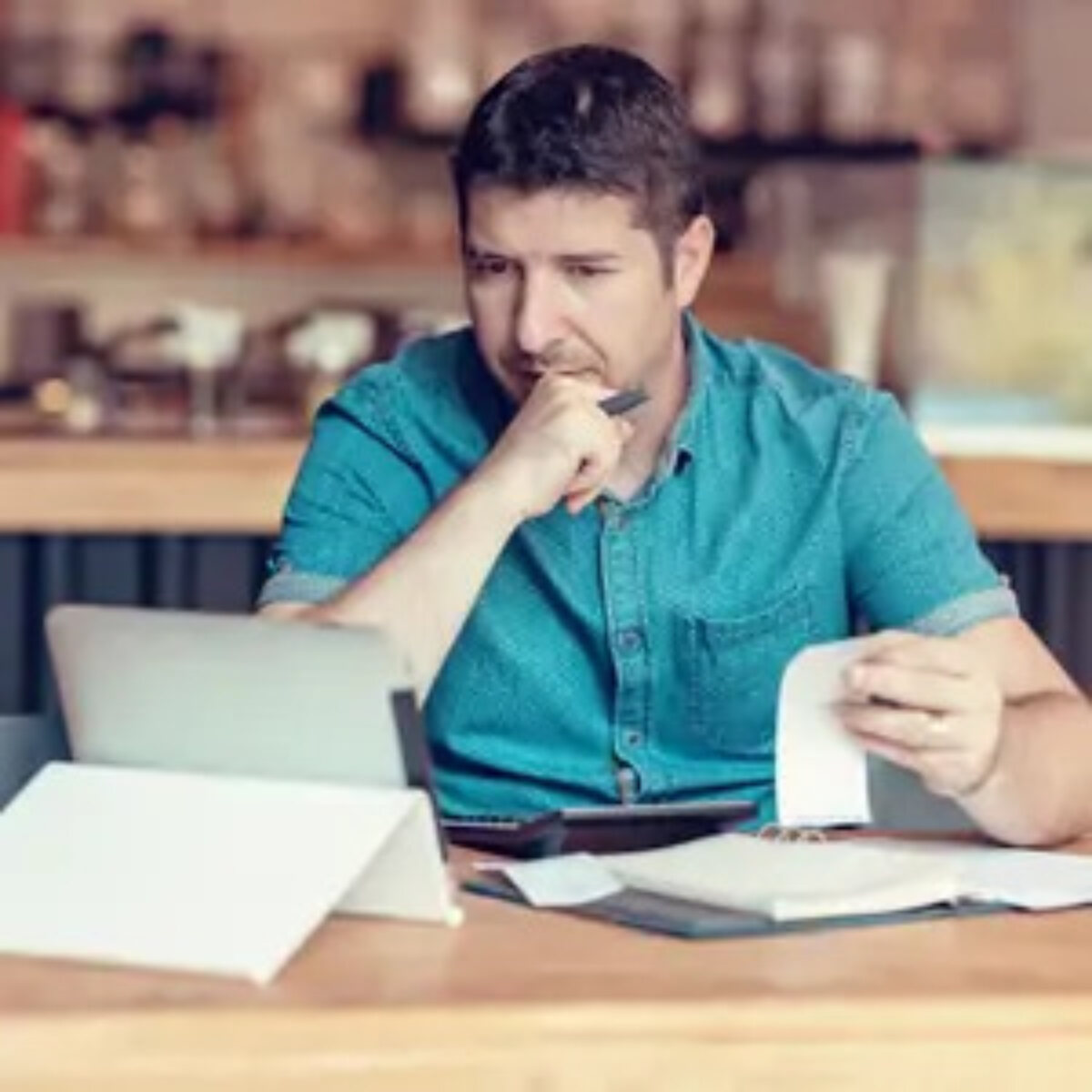 SME owner making calculations with receipts, tablet and calculator at table in cafe