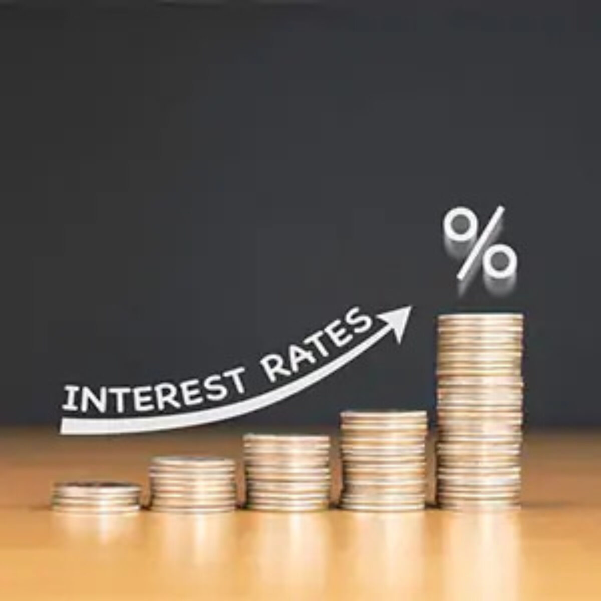 Five stacks of coins increasing in height with an image of an upward arrow with the words 'interest rates' above it and a percentage symbol above the tallest stack