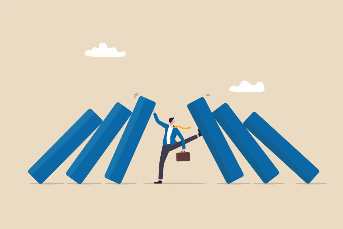 Cartoon of miniature businessman with books falling inwards on either side, holding them up with his hand on one side and his foot on the other