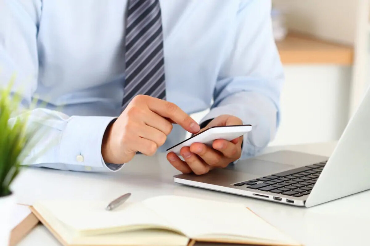 Businessman using smartphone in front of open laptop