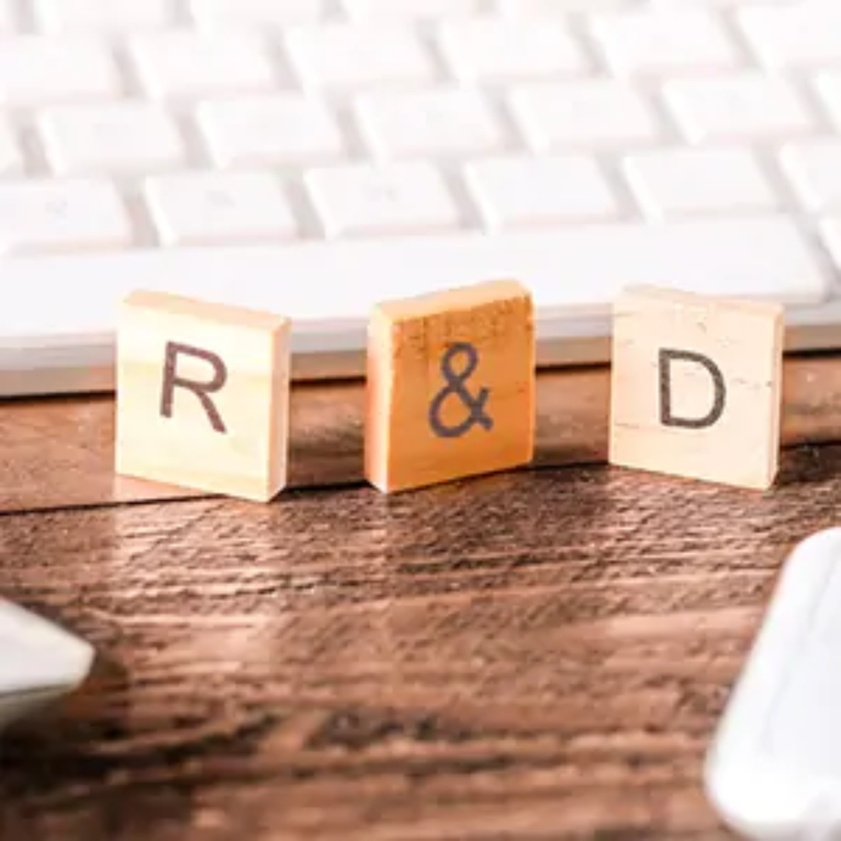 Wooden scrabble-style tiles balanced upright in front of computer keyboard spelling out R&D
